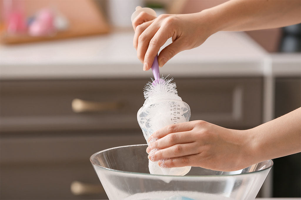 Person’s hands cleaning baby bottles in the kitchen.