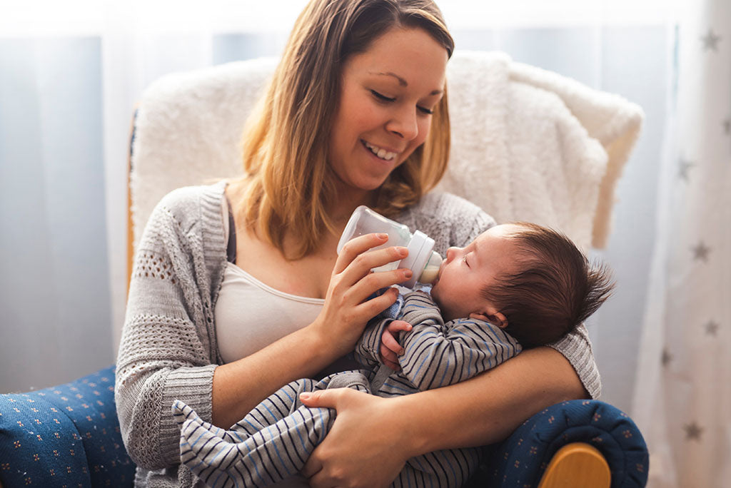 Happy young mother feeding her infant son from a bottle.