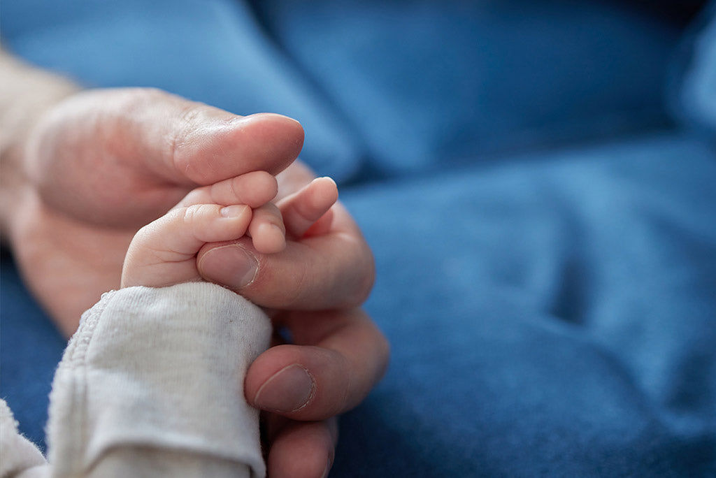 Closeup of a father’s hand holding a newborn’s hand. 