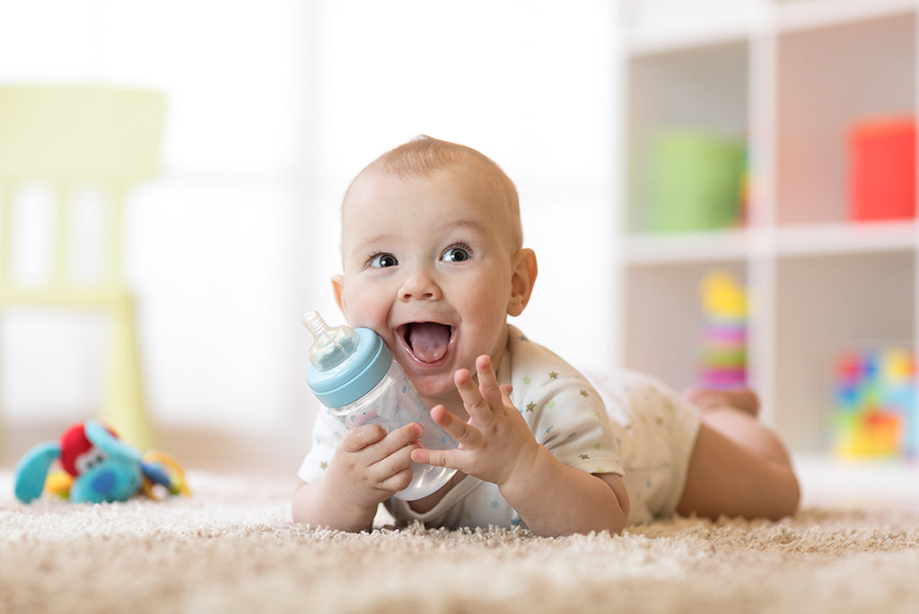 Smiling baby closeup holding a baby bottle.