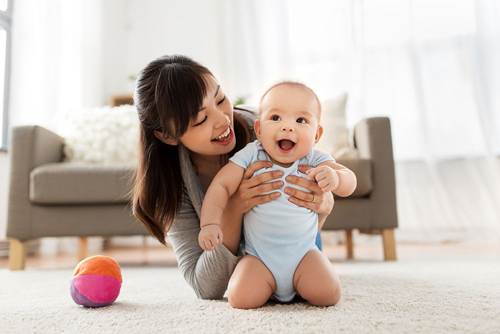 Young asian mom holding her smiling baby on the floor.