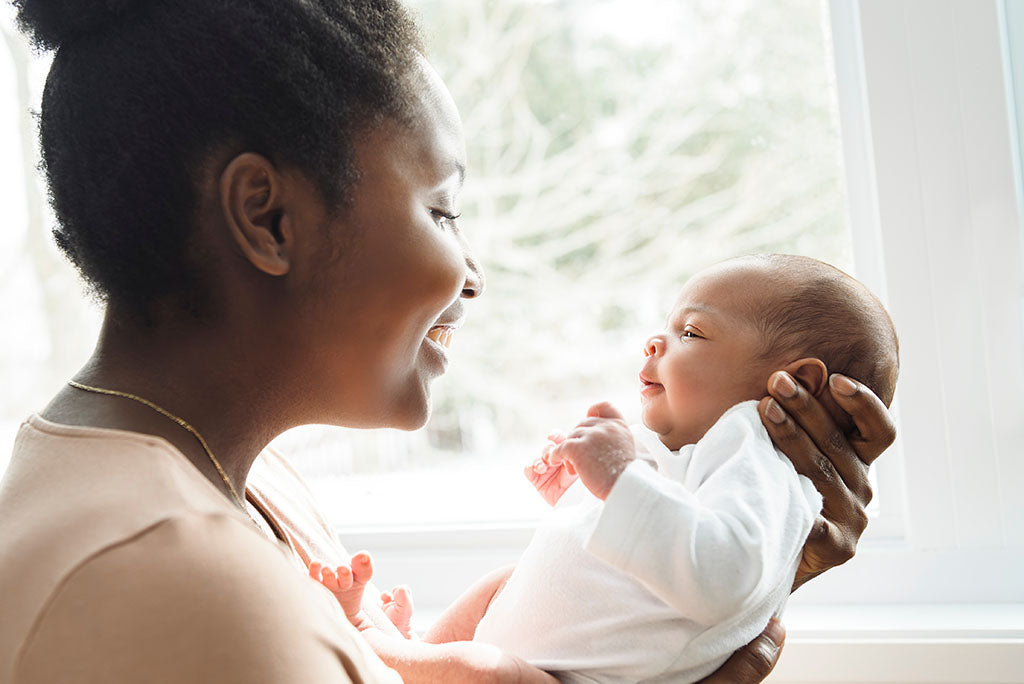 Young mother holding her newborn infant in front of a window. 